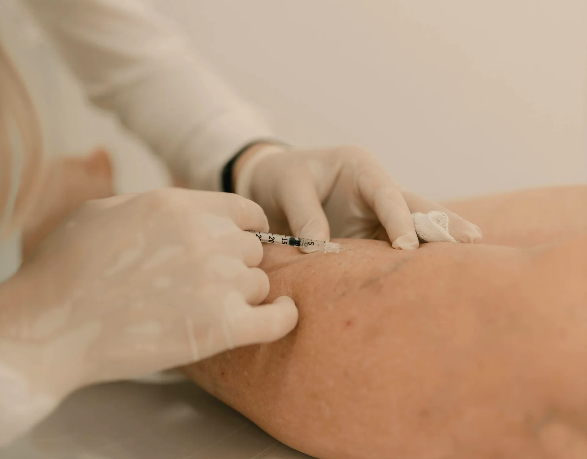 Nurse or clinician wearing gloves administers a syringe injection into a patient&rsquo;s upper arm, with a small bandage nearby.
