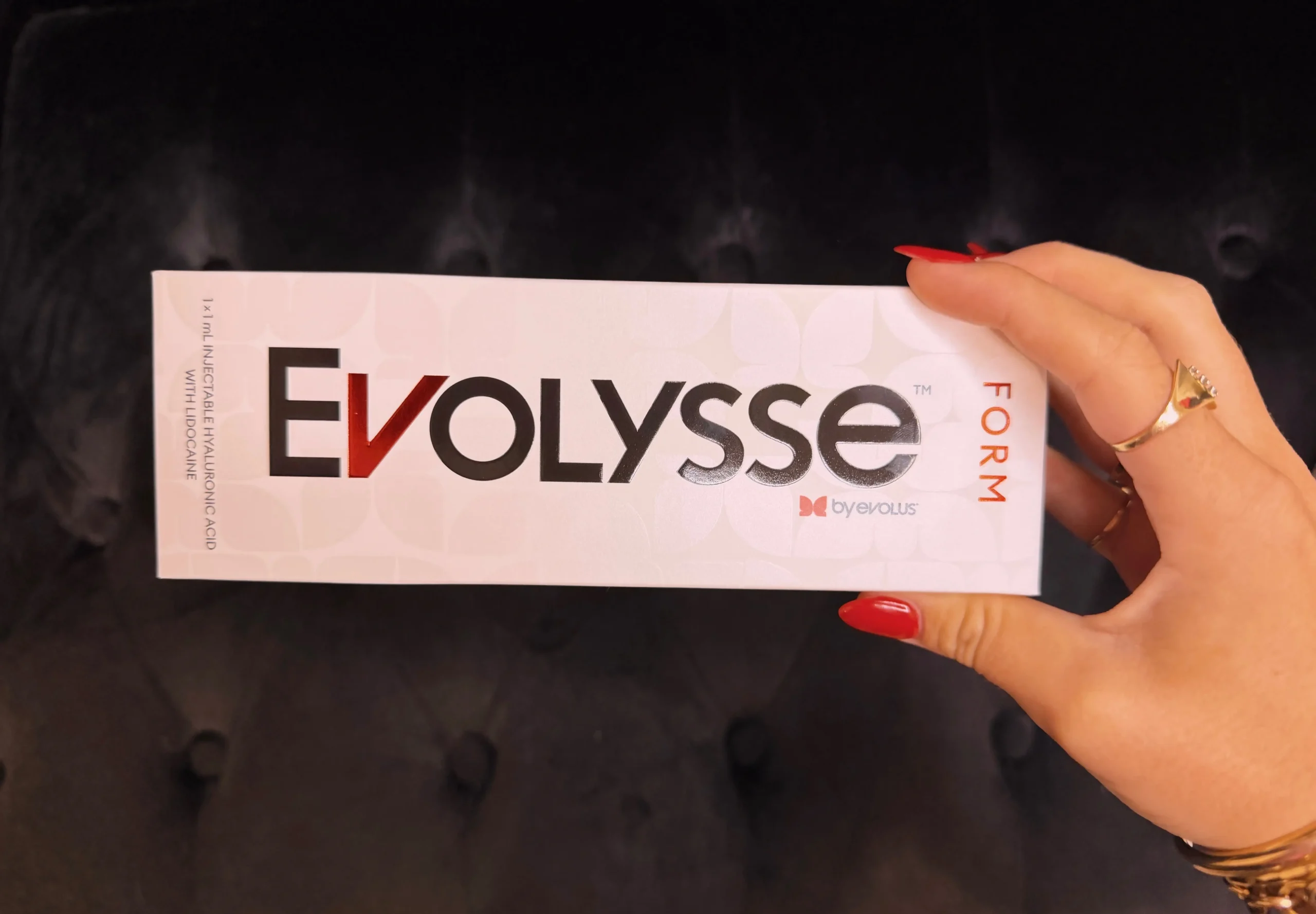 Hand with red nails holding a white Evolyse box, showing the brand name and the note '1 x 1 mL Injectable Hyaluronic Acid with Lidocaine' along the side.