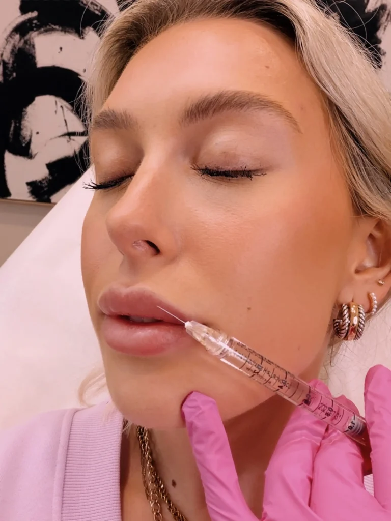 Close-up of a patient with eyes closed while a clinician in pink gloves administers a syringe near the mouth.