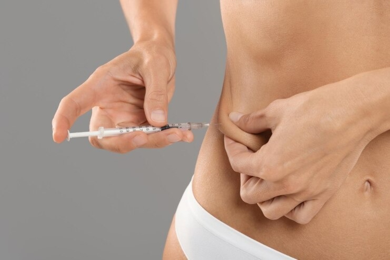 Close-up of hands administering a syringe into the abdomen, suggesting an injection (likely insulin) into the skin.