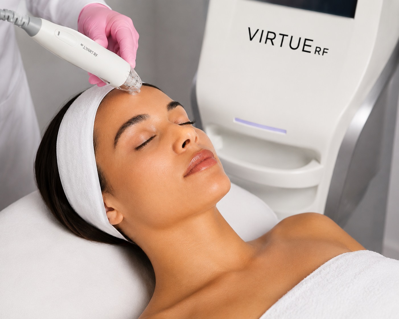 Woman receiving a cosmetic facial treatment with a handheld RF device on her forehead while lying with eyes closed, headband in place.