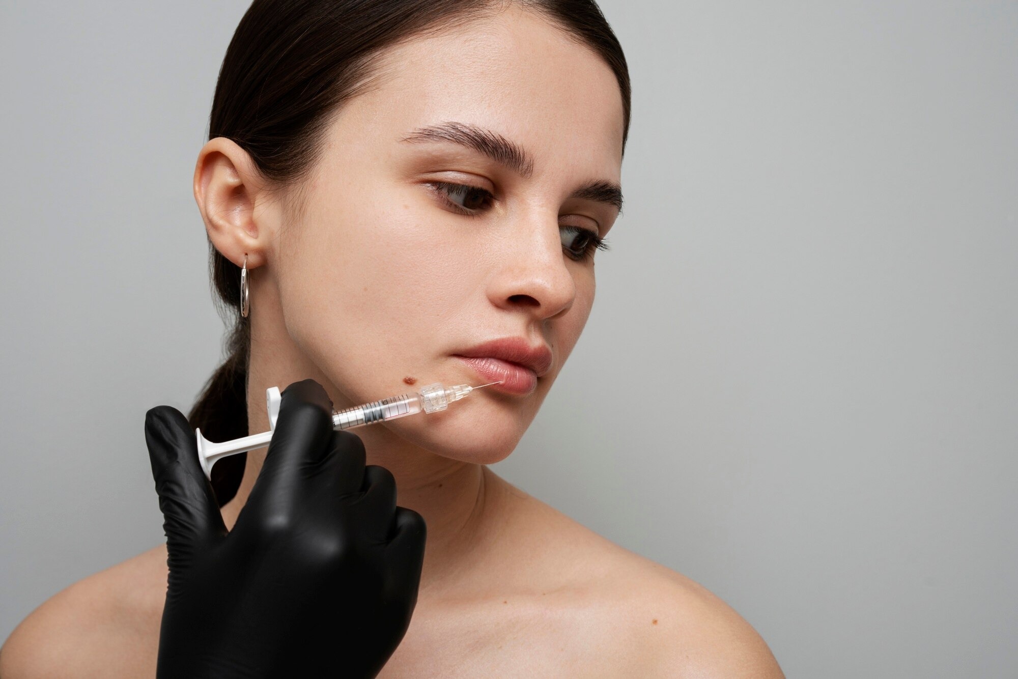 Close-up of a woman receiving a cosmetic lip injection from a clinician in black gloves.