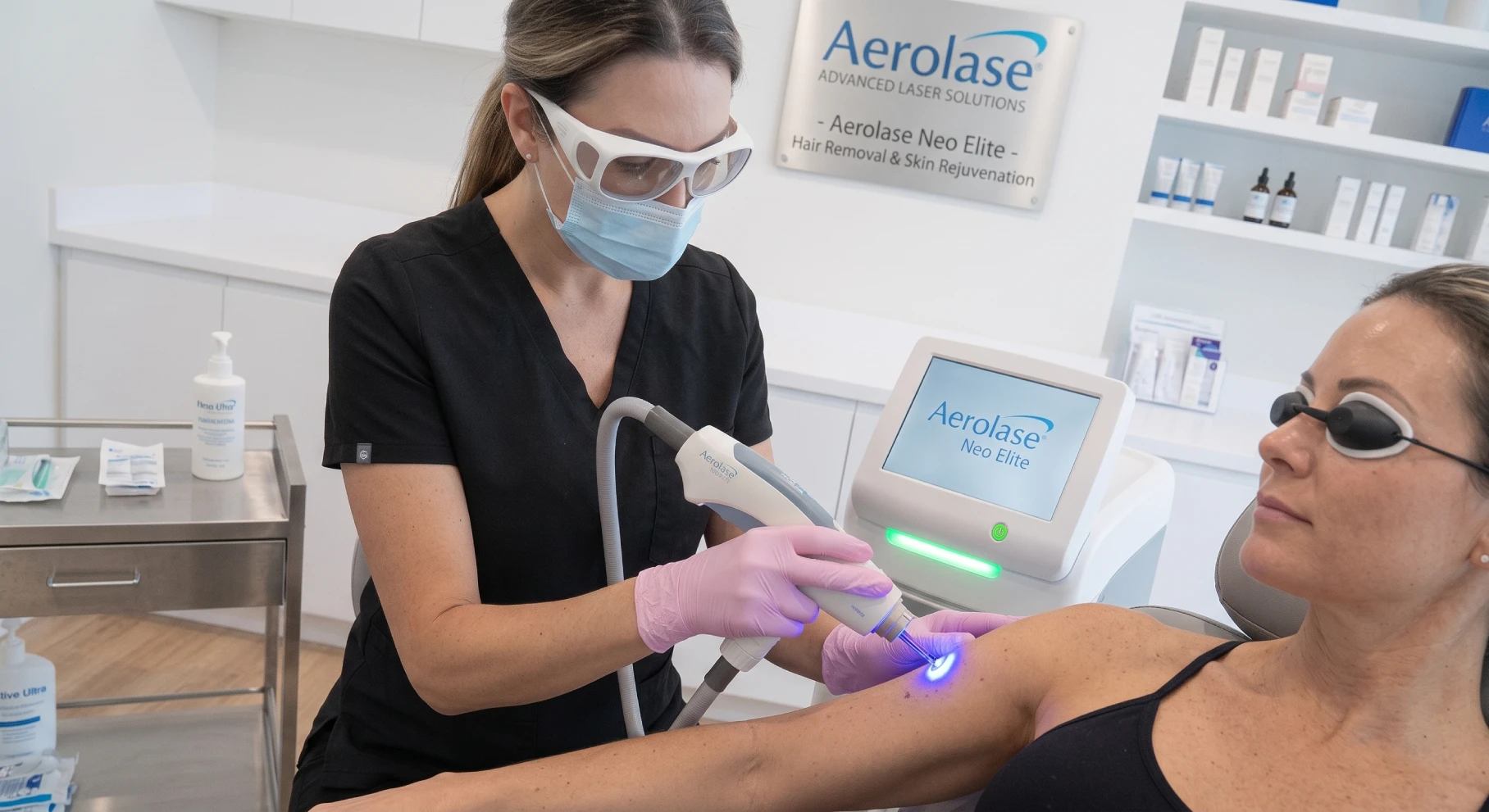 Clinician in a mask and goggles performs laser treatment on a patient’s shoulder using the Aerolase Neo Elite device in a bright clinic.